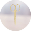 A pair of small, gold-colored scissors with rounded handles, displayed upright against a soft, blurred background.