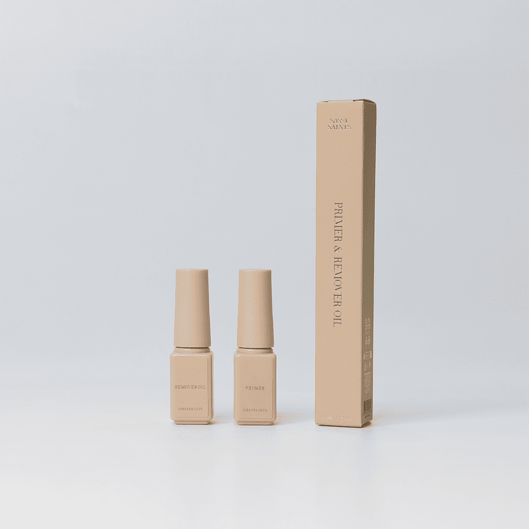 Sassy Saints - Brings The Salon Home presents Primer & Remover Oil (FREE) in minimalist beige bottles with a matching tall box, all set against a plain white background for an elegant look.