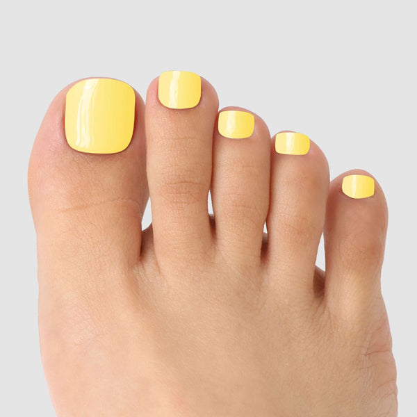 A close-up of toes with glossy Buttercup Yellow Pedicure Gel Wraps by Sassy Saints - Brings The Salon Home, set against a plain light gray background.